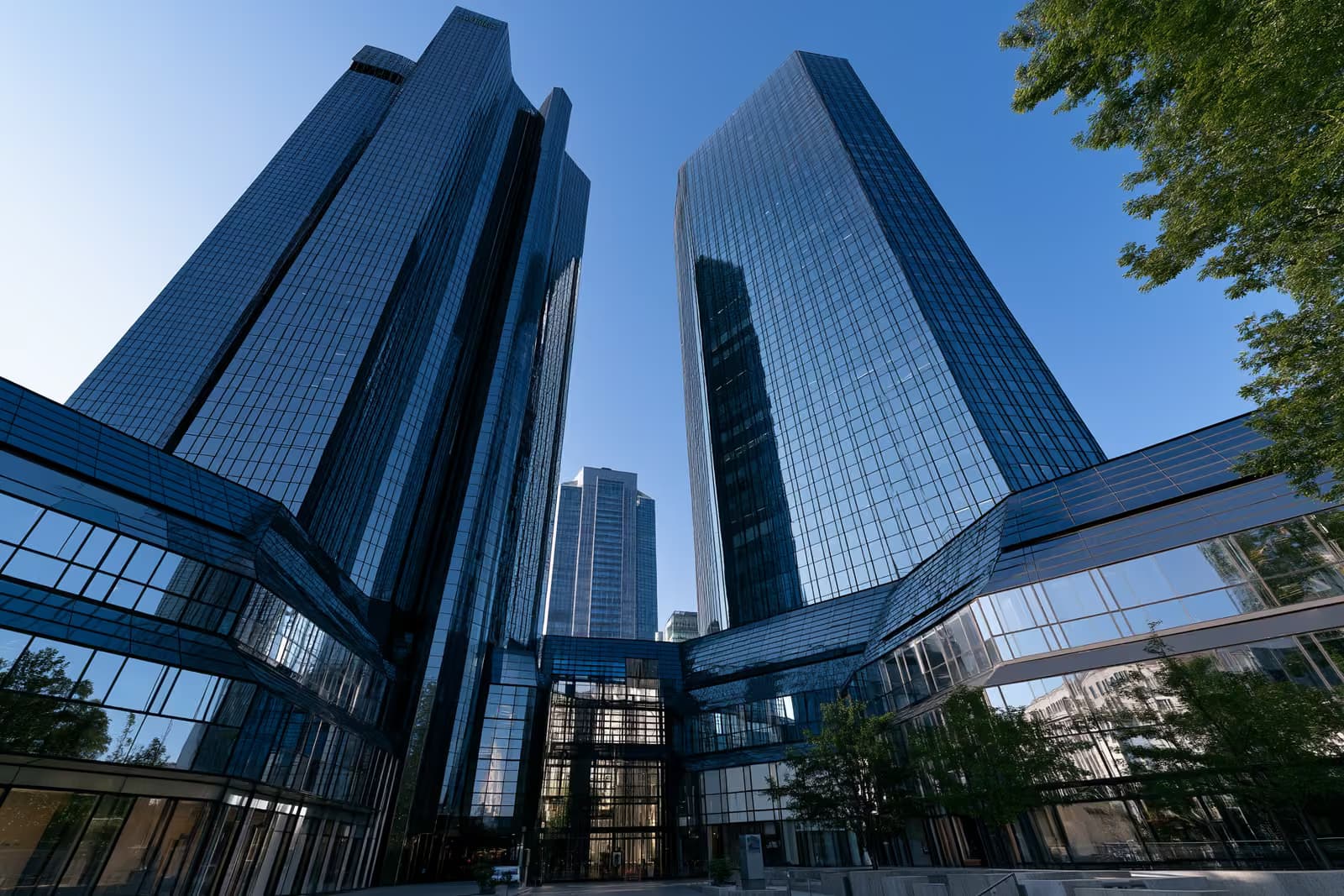 Frankfurt'taki ikiz cam banka kuleleri, aşağıdan bakıldığında parlak mavi bir gökyüzüne karşı ışıldıyor.